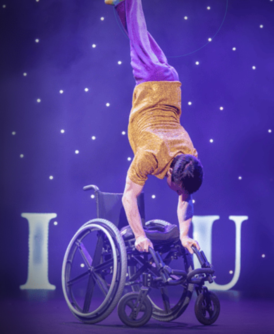 Omnium Circus performer doing a handstand on a wheelchair under stage lights